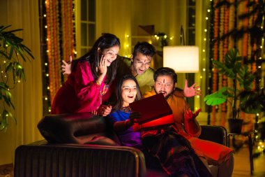 Hintli aile veya genç çiftler Diwali 'yi evde kutluyorlar, koltukta oturuyorlar, parlayan sürpriz bir hediye kutusu açıyorlar, Hindu bayramı boyunca birlikte neşe ve heyecan paylaşıyorlar.