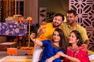 Mutlu Hintli çiftler ve geleneksel arkadaşlar Diwali 'yi evde içeceklerle, tatlılarla, hediyelerle, çiçeklerle, selfie çekerek ve birlikte eğlenerek kutlarlar..