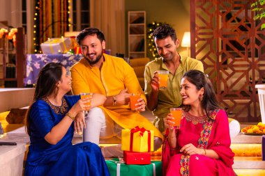 Mutlu Hintli çiftler ve geleneksel arkadaşlar Diwali 'yi evde içeceklerle, tatlılarla, hediyelerle, çiçeklerle, selfie çekerek ve birlikte eğlenerek kutlarlar..