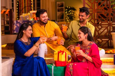 Mutlu Hintli çiftler ve geleneksel arkadaşlar Diwali 'yi evde içeceklerle, tatlılarla, hediyelerle, çiçeklerle, selfie çekerek ve birlikte eğlenerek kutlarlar..