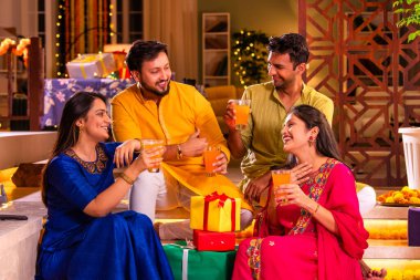 Mutlu Hintli çiftler ve geleneksel arkadaşlar Diwali 'yi evde içeceklerle, tatlılarla, hediyelerle, çiçeklerle, selfie çekerek ve birlikte eğlenerek kutlarlar..