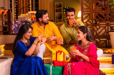 Mutlu Hintli çiftler ve geleneksel arkadaşlar Diwali 'yi evde içeceklerle, tatlılarla, hediyelerle, çiçeklerle, selfie çekerek ve birlikte eğlenerek kutlarlar..