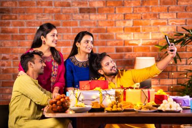 Mutlu Hintli çiftler ve geleneksel arkadaşlar Diwali 'yi evde içeceklerle, tatlılarla, hediyelerle, çiçeklerle, selfie çekerek ve birlikte yemek masasında oturarak kutluyorlar.
