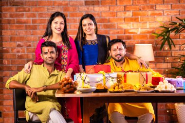 Mutlu Hintli çiftler ve geleneksel arkadaşlar Diwali 'yi evde içeceklerle, tatlılarla, hediyelerle, çiçeklerle, selfie çekerek ve birlikte yemek masasında oturarak kutluyorlar.