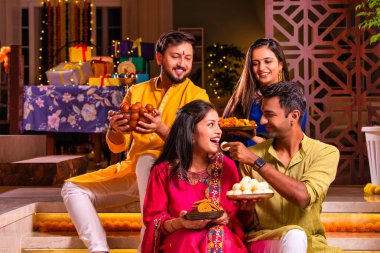 Mutlu Hintli çiftler ve geleneksel arkadaşlar Diwali 'yi evde içeceklerle, tatlılarla, hediyelerle, çiçeklerle, selfie çekerek ve birlikte eğlenerek kutlarlar..