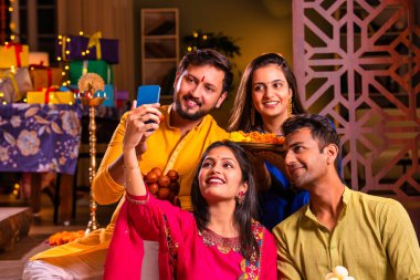 Mutlu Hintli çiftler ve geleneksel arkadaşlar Diwali 'yi evde içeceklerle, tatlılarla, hediyelerle, çiçeklerle, selfie çekerek ve birlikte eğlenerek kutlarlar..
