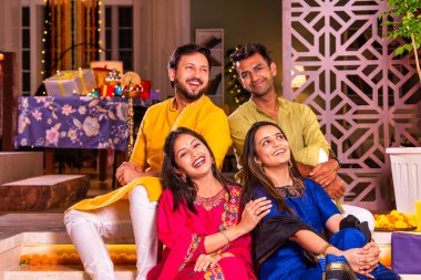 Mutlu Hintli çiftler ve geleneksel arkadaşlar Diwali 'yi evde içeceklerle, tatlılarla, hediyelerle, çiçeklerle, selfie çekerek ve birlikte eğlenerek kutlarlar..