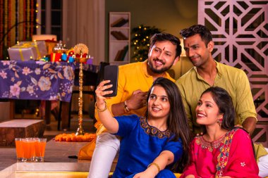 Mutlu Hintli çiftler ve geleneksel arkadaşlar Diwali 'yi evde içeceklerle, tatlılarla, hediyelerle, çiçeklerle, selfie çekerek ve birlikte eğlenerek kutlarlar..