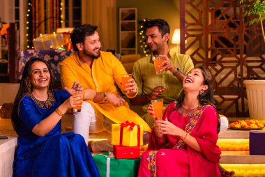 Mutlu Hintli çiftler ve geleneksel arkadaşlar Diwali 'yi evde içeceklerle, tatlılarla, hediyelerle, çiçeklerle, selfie çekerek ve birlikte eğlenerek kutlarlar..