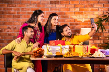 Mutlu Hintli çiftler ve geleneksel arkadaşlar Diwali 'yi evde içeceklerle, tatlılarla, hediyelerle, çiçeklerle, selfie çekerek ve birlikte yemek masasında oturarak kutluyorlar.