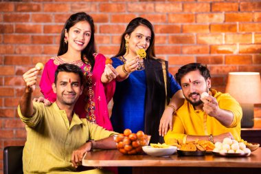 Mutlu Hintli çiftler ve geleneksel arkadaşlar Diwali 'yi evde içeceklerle, tatlılarla, hediyelerle, çiçeklerle, selfie çekerek ve birlikte yemek masasında oturarak kutluyorlar.