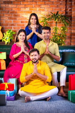 Geleneksel Hint elbiseli neşeli Asyalı çiftler Diwali 'yi evde kutluyorlar, bir kanepede oturuyorlar, Namaste veya Namaskar ile konukları selamlıyorlar, kutlama vesilesinin keyfini çıkarıyorlar sevgi ve saygıyla.