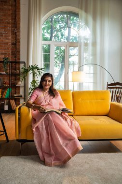 Göz kamaştırıcı bir sariyle güzel yaşlı bir Hintli kadının portresi, bir kanepede rahatça otururken kendine güven ve sükunet yayıyor, kitap ya da roman okuyor, karamsar bir ışıkta yakalanmış.