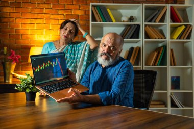 Asyalı Hintli yaşlı çift, emeklilik yatırımlarını dizüstü bilgisayarda gözden geçiren hayal kırıklığına uğramış yüzleriyle, borsadaki düşüşten endişe duyuyorlar.