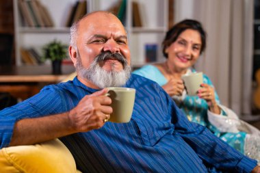 Emekli Hintli çift evdeki kanepede rahat bir anın tadını çıkarıyorlar. En sevdikleri çayı ya da kahveyi yudumluyorlar ve tatlı sohbetlerini paylaşıyorlar.
