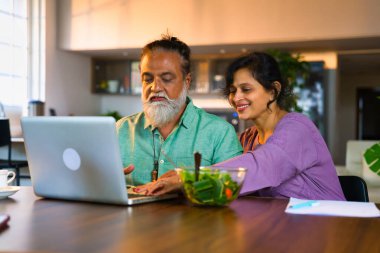 Hindistan 'da orta yaşlı bir çift birlikte ev ekonomisi üzerinde çalışıyor, koca dizüstü bilgisayar kullanıyor, karısı ise pahalı evlerinde kalem, kağıt ve hesap makinesiyle not alıyor.