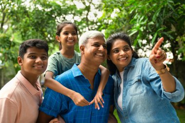 Dört kişilik Hintli Asyalı bir aile, 40 'larında ebeveynleri ve iki küçük çocuğu olan, açık havada bir anın tadını çıkaran, gülümseyen ve uzaktaki bir şeye işaret eden, birlikte mutluluğu paylaşan