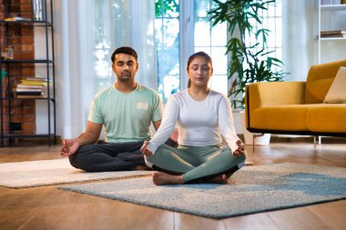 Hintli Asyalı genç çift online yoga dersini takip ederek mutlu bir şekilde meditasyon, pranayam ve nefes egzersizleri yaparak müsrif evlerinde oturuyorlar.