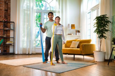 Hint Asyalı genç çift ya da spor kıyafeti giymiş arkadaşlar birlikte egzersiz yapmak için direniş bantlarını kullanıyorlar. Ya ayakta duruyorlar ya da modern bir stüdyoda oturuyorlar.