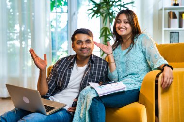 Hintli Asyalı genç bir çift gösterişli bir evde sarı bir kanepeye oturmuş, mali durumlarını birlikte idare ederken gülümsüyorlardı, bir dizüstü bilgisayar ve belgeleri bütçe ve gider planlaması için kullanıyorlardı.