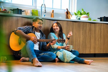 Neşeli Hintli, Asyalı genç çift mutfak zemininde oturmuş gitar akorlarını dinlendiriyorlar ve tıngırdatarak birlikte şarkı söylüyorlar..