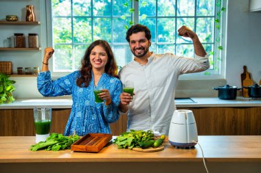 Hintli çift mutfakta birlikte taze yeşil ıspanak suyu hazırlıyor. İkisi de sağlık ve zindeliği destekleyen güçlü bir hareket sergiliyor.