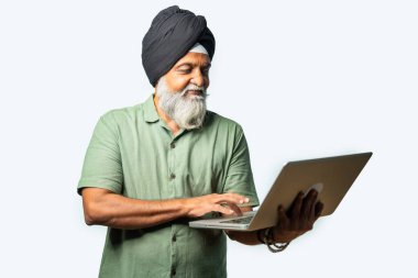 Mutlu ve kendinden emin Hintli Asyalı YaşIı Sikh Adam, Beyaz Arkaplan 'a Karşı Ayakta Dururken Dizüstü bilgisayar kullanıyor, Başarı, Düşünme veya Gösterme