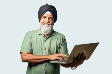 Mutlu ve kendinden emin Hintli Asyalı YaşIı Sikh Adam, Beyaz Arkaplan 'a Karşı Ayakta Dururken Dizüstü bilgisayar kullanıyor, Başarı, Düşünme veya Gösterme