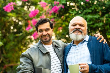 Mutlu Hintli Asyalı Baba ve Genç Yetişkin Oğul Ev Bahçesinde Yürürken, Kahvenin keyfini çıkarırken, Gülüşürken ve Konuşurken Birlikte Neşeli, Neşeli Bir Anda