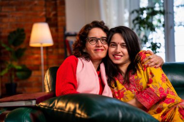 Mutlu bir Hintli genç kızın yakından çekilmiş portresi. 20 'li yaşlarda güzel bir Hintli kız ve 50' li yaşlarda annesi. İkisi de evdeki rahat bir kanepede yan yana oturup eğlenirken kameraya bakıyor..