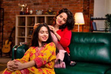 50 'li yaşlarda Hintli bir Asyalı anne, evdeki bir kanepede oturup sevgi ve şefkat gösterirken güzel genç kızına sevgiyle masaj yapıyor.