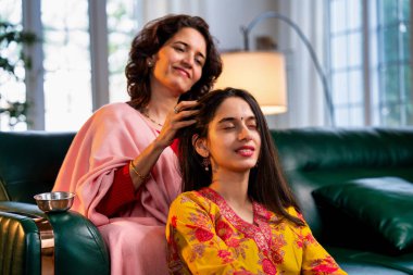 50 'li yaşlarda Hintli bir Asyalı anne, evdeki bir kanepede oturup sevgi ve şefkat gösterirken güzel genç kızına sevgiyle masaj yapıyor.