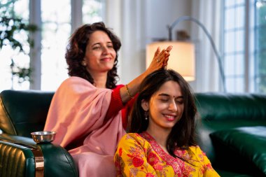 50 'li yaşlarda Hintli bir Asyalı anne, evdeki bir kanepede oturup sevgi ve şefkat gösterirken güzel genç kızına sevgiyle masaj yapıyor.