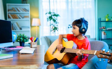 Evde Masaüstü Bilgisayarı Kullanarak İnternetten Asyalı Çocuk Akustik Gitar Öğreniyor