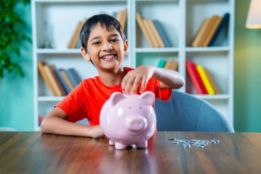 Hindistan Küçük Çocuğu Modern Ev 'de Masada Oturuyor, Piggy Bank' a veya Para Kutusuna Para Koyarak Para Tasarruf Ediyor, Mali Sorumluluk Öğreniyor, Erken Yaştan Tasarruf kavramı