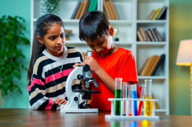 Hint Asyalı, şirin küçük kız ve oğlan öğrencileri Modern Sınıfta Masa 'da oturuyorlar, Mikroskop kullanarak oyun oynuyorlar, deney tüplerinde kimyasal çözümler kullanıyorlar, kimya öğreniyorlar.