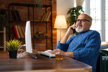 Kurta 'daki teknoloji meraklısı Hintli emekli adam masaüstü bilgisayarını kullanıyor, telefonla konuşuyor, kahveyi yudumluyor, birden fazla iş yapıyor ve kendi masasında otururken üretken kalıyor.