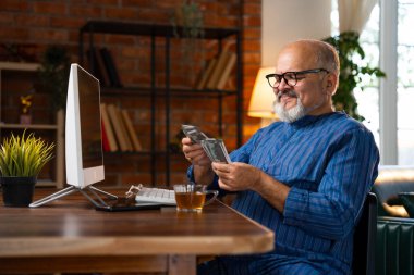 Kurta 'daki Hintli kıdemli emekli adam evde bilgisayarın başında oturmuş, odaklanarak finansmanı yönetirken 500 rupi sayıyor.