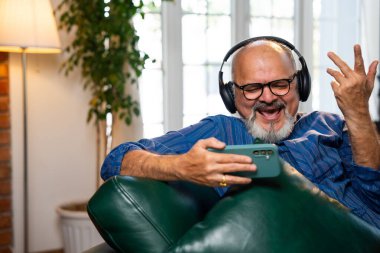 Hintli emekli, sakallı, kurta giyen, yüksek sesle gülen, akıllı telefonlu, kablosuz kulaklıklı komik videolar izleyen, eğlencenin tadını çıkaran yaşlı bir adam.