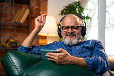 Hintli emekli, sakallı, kurta giyen, yüksek sesle gülen, akıllı telefonlu, kablosuz kulaklıklı komik videolar izleyen, eğlencenin tadını çıkaran yaşlı bir adam.