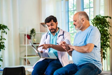 Hintli Asyalı erkek doktor bilek ağrısı teşhisini, tedavi seçeneklerini ve OPD 'deki yaşlı bir hastaya iyileşme sürecini açıklayarak, rahat bir klinikte kaliteli sağlık ve hasta bilincini güvence altına alıyor.