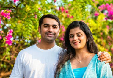 Hintli Asyalı genç ve güzel bir çift, sıcak bir sabah güneşi altında doğada yürürken neşeli anları paylaşıyor, gülüyor, sarılıyor ve barışçıl ve romantik bir doğa yürüyüşünün tadını çıkarıyorlar.