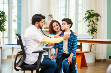 Hintli Asyalı erkek doktor, modern klinikte genç erkek çocuklarına steteskop kullanarak genel semptomları kontrol ediyor.