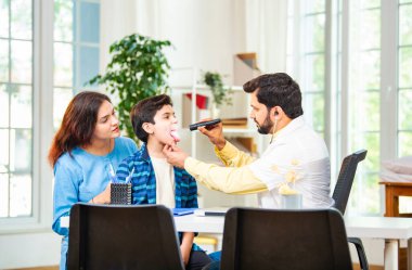 Hintli Asyalı erkek doktor, modern klinikte genç erkek çocuklarına steteskop kullanarak genel semptomları kontrol ediyor.