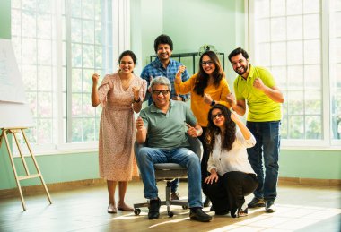 Modern girişim ofisindeki Hintli Asyalı genç şirket profesyonelleri, şık giyinmiş, el çırpıyor, başarıyı, başarıyı, takım çalışmasını, yeniliği, iş büyümesini kutluyorlar.