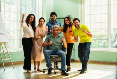 Modern girişim ofisindeki Hintli Asyalı genç şirket profesyonelleri, şık giyinmiş, el çırpıyor, başarıyı, başarıyı, takım çalışmasını, yeniliği, iş büyümesini kutluyorlar.