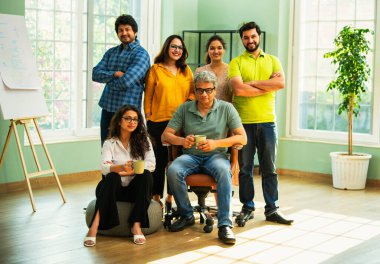 Genç girişimcilerden oluşan Hint Asya dinamik ekibi modern yaratıcı ofiste başarıyı kutluyor. Kameraya, takım çalışmasına, lidere gülümseyen iş adamlarına güveniyorlar.