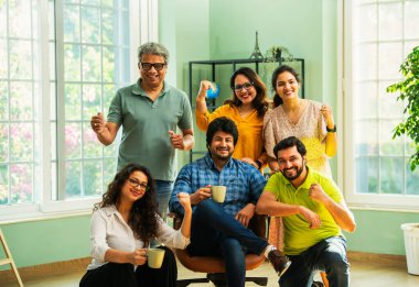 Modern girişim ofisindeki Hintli Asyalı genç şirket profesyonelleri, şık giyinmiş, el çırpıyor, başarıyı, başarıyı, takım çalışmasını, yeniliği, iş büyümesini kutluyorlar.