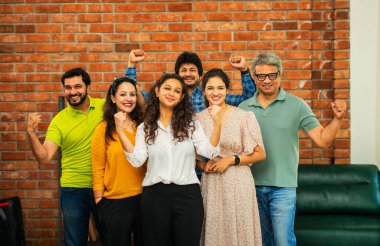 Genç girişimcilerden oluşan Hint Asya dinamik ekibi modern yaratıcı ofiste başarıyı kutluyor. Kameraya, takım çalışmasına, lidere gülümseyen iş adamlarına güveniyorlar.