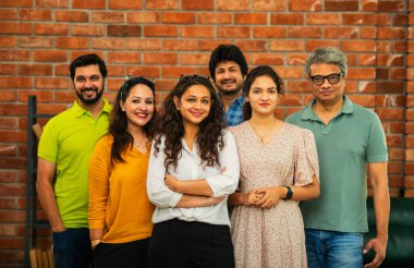 Hint Asya dinamik girişim ekibi genç girişimcilerden oluşan akıllı girişimciler modern yaratıcı ofiste bir arada duruyorlar kameraya, takım çalışmasına, lidere gülümseyen iş adamlarına güveniyorlar.